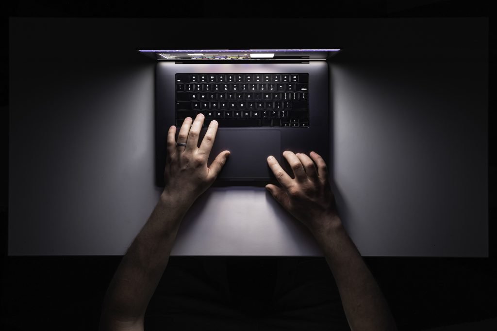 Man using laptop at night, workplace, top view. Minimalistic workplace, working with computer, using laptop at night and online privacy concept.